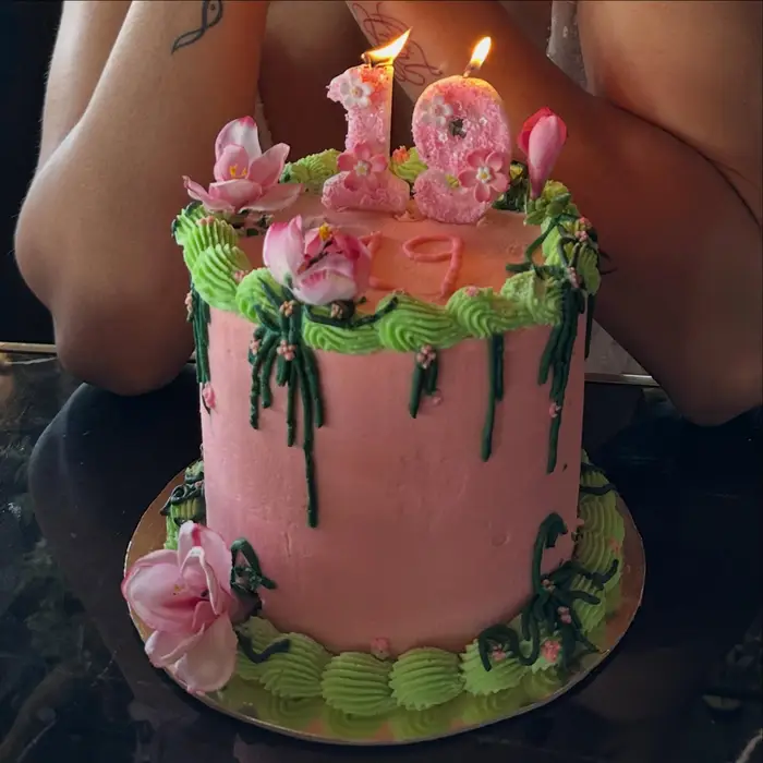 A pink drip cake with buttercream flowers and lit number one candles