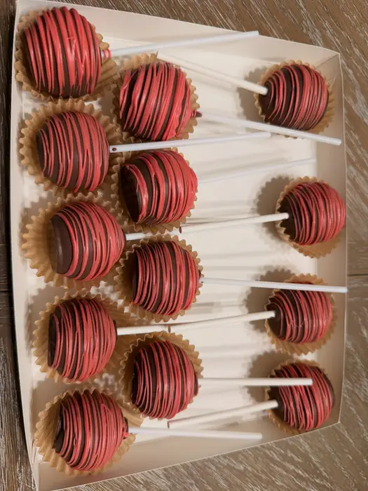 A boxed tray of chocolate cake pops with red drizzle