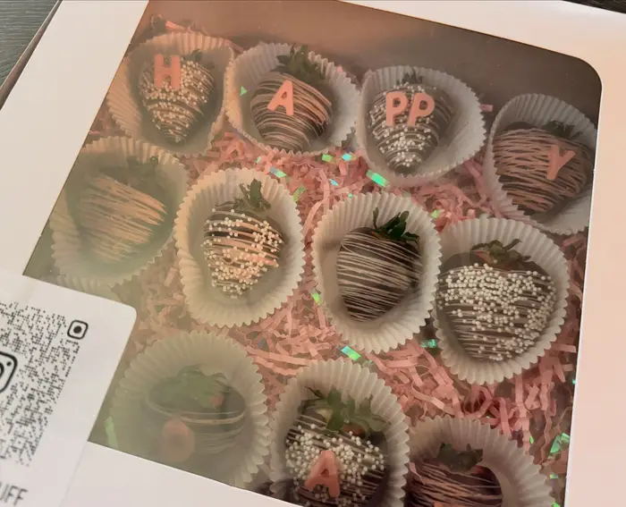 A boxed set of chocolate dipped strawberries with pink lettering